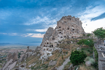 Fototapeta na wymiar Uchisar Castle in Cappadocia, Turkey with balloons in background