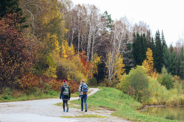 Two young women with backpacks are on the path. Autumn landscape