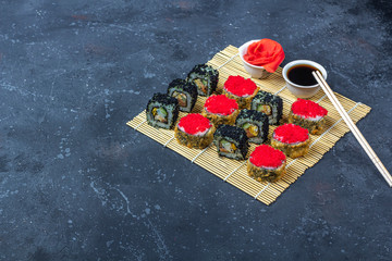 Set of sushi roll with omelet, tofu and vegetables, flying fish roe, tempura on makisu on a dark background. Traditional Japanese food. Top view, flat lay, copy space for text.