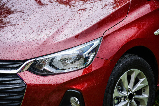 Detalhe do farol de um carro vermelho, molhado