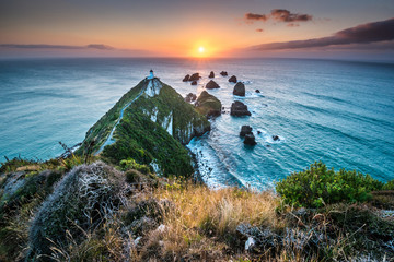 Nugget point. Rock Cliffs and Lighthouse in the South Island. Magical colorful daybreak on rock cliffs with lighthouse in Otago district close to Dunedin, South Island of New Zealand. Sun rays and bea