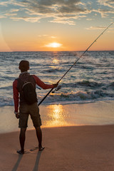 Fisherman stands on sandy beach during sunset
