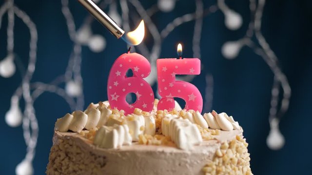 Birthday cake with 65 number pink candle on blue backgraund. Candles are set on fire. Slow motion and close-up view
