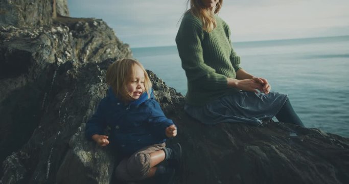 Young mother sitting on rock by the sea with her toddler