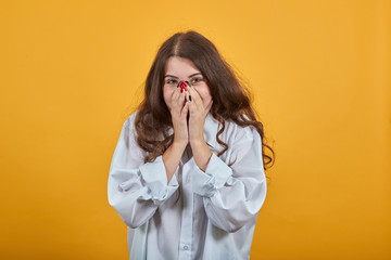 Smiling caucasian young woman in fashion white shirt covering mouth with hands, smiling isolated on orange background in studio. People sincere emotions, lifestyle concept.