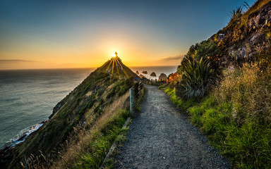 Sunrise on Nugget Point with sun rays shinning over lighthouse.