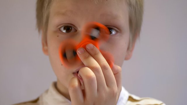 Funny blond child in striped shirt twists spinner on his nose. Portrait of boy on white background. 4K. Soothing toy. Autism. Exercise for preschoolers. Falling soap bubbles