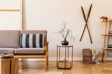 Stylish interior design of living room at cozy apartment with brown sofa, coffee table, wooden cube, vase, pillow and elegant accessories. Minimalistic concept of home staging. Beige wall. Template.