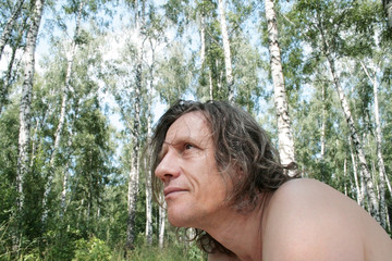 An elderly man with long hair in a birch grove looks carefully. Russian