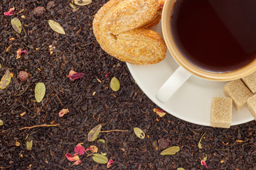 white mug with hot black tea with  cookies on a white saucer on the background of black loose tea top view