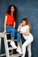 young pretty teenage girls friends with blond and brunette curly hair posing cheerful on blue background, lifestyle people concept