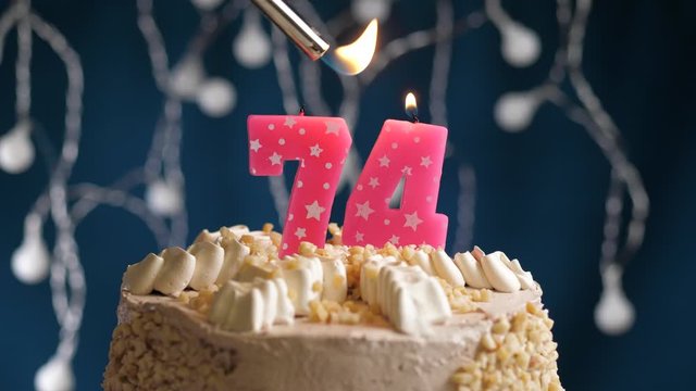 Birthday cake with 74 number pink candle on blue backgraund. Candles are set on fire. Slow motion and close-up view