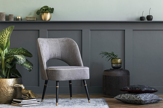 Modern composition of living room with design gray armchair, furniture, gold pot with beautiful plant and elegant personal accessories. Gray wall panelling with shelf. Stylish home staging. Template. 