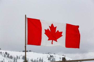 Canadian Flag with a white winter mountain landscape in the background during a foggy morning. Taken in Whistler, British Columbia, Canada.