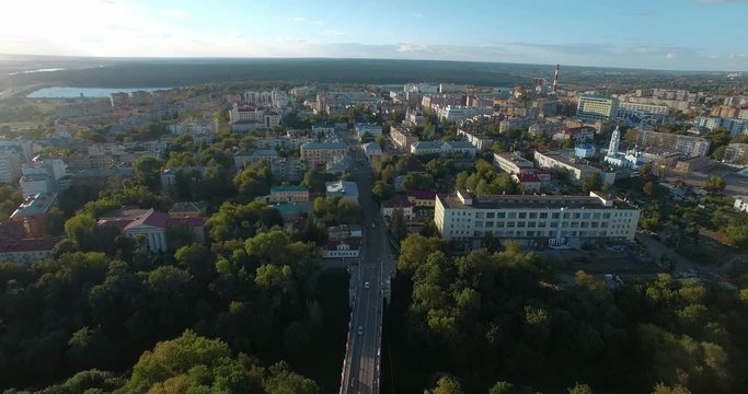 Flying over Russian city Kaluga in sun light. Aerial view of streets and buildings surrounded with green woods