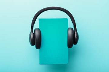 Headphones are worn on a book in a blue hardcover on a blue background, top view.