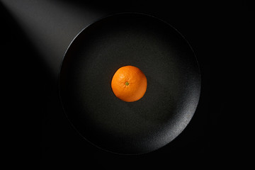 Tangerine in black plate on black background with ray of light