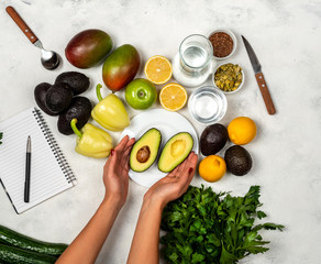 The girl cut the avocado into two parts. Preparing fruits and vegetables for a delicious meal. Top view.