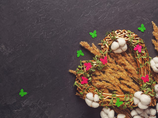 Romantic composition for Valentine's Day. A golden wicker heart is on a dark background. Decorating with dried plants, cotton flowers and colorful felt butterflies. Flat lay. Copyspace.