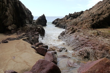 Fototapeta na wymiar Bachmündung ins Meer mit Felsen und Sand