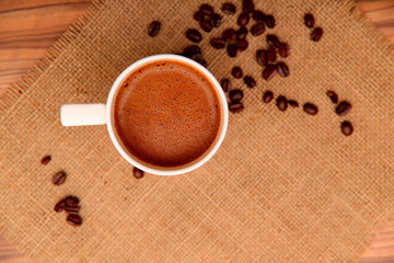 On the burlap grains of roasted coffee and a white cup of coffee. Top view, free space, horizontal, close-up. Coffee concept.
