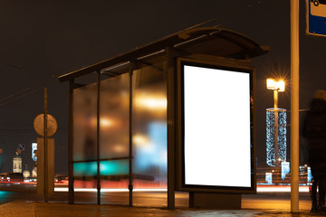 Billboard in a stop. White field for advertising glowing at night in the city. Vertical Field Mockup glass stop passing by blurry cars with people in the background