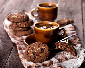 Two cups of coffee and chocolate chip cookies on rustic wooden background.
