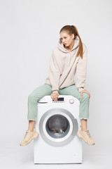 Portrait of young beautiful young girl sitting on a washing machine and looking at the camera isolated on white background
