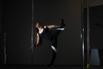 The dancer on the pylon in the studio. Girl doing exercises on a sports equipment.
