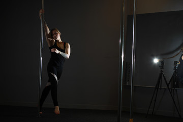 Fototapeta na wymiar The dancer on the pylon in the studio. Girl doing exercises on a sports equipment.