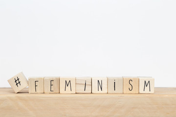 Wooden cubes with a hashtag and the word Feminism near white background, social media concept