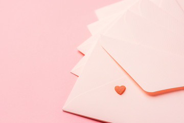 Pink envelopes arranged in fan with one small red candy heart on top on monochrome pastel...