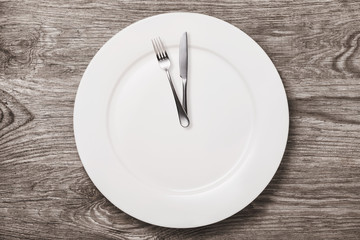 Empty ceramic plate and cutlery on a wooden table, top view. Concept on the topic: time to eat
