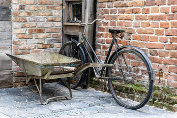 Fototapeta na wymiar A black old bicycle and wheelbarrow are standing by a brick wall