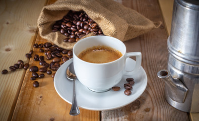 coffee in ceramic cup, moka coffee machine, coffee beans and burlap sack on wooden background
