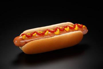 Classic hot dog with ketchup and mustard on a black background. - obrazy, fototapety, plakaty