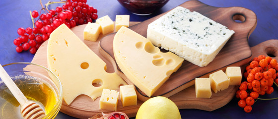 Cheese platter: variety of cheeses on wooden plate with fruits. Different types of cheese and honey. Hard cheese and berries on a classic blue background. Top view