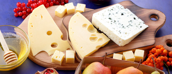 Cheese platter: variety of cheeses on wooden plate with fruits. Different types of cheese and honey. Hard cheese and berries on a classic blue background. Top view