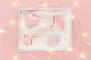 gift box with rose quartz jade roller and stone on pastel pink background with festive lights