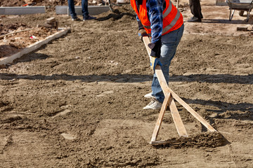 A worker levels the sand foundation with a wooden level for subsequent laying of tiles on the sidewalk.