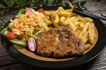 Fried pork chop in breadcrumbs, served with fries and salad.
