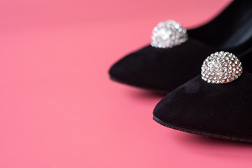 close-up black suede women's shoes with rhinestone embellishments on a pink background