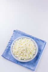 Cottage cheese in a white plate. Fresh cottage cheese on a white background. Homemade curd on a blue napkin in minimalist style. Top view. Copy space