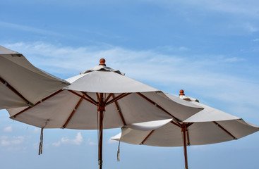 White canvas beach umbrellas shot against light blue sky and clouds. 
