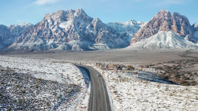 Aerial pullback shot of cars, snow desert mountain landscape in Red Rock Canyon