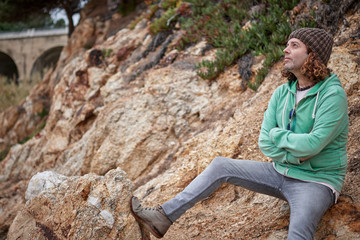 a middle-aged man with youthful style sitting on some rocks
