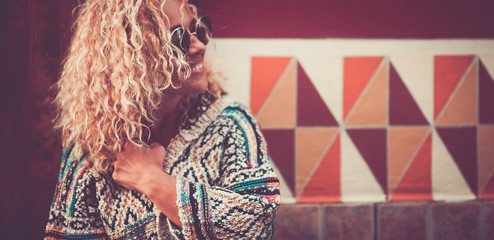 Portrait in vintage colors of cheeful beautiful curly blonde lady with red wall in background - happy adult people in outdoor leisure activity alone