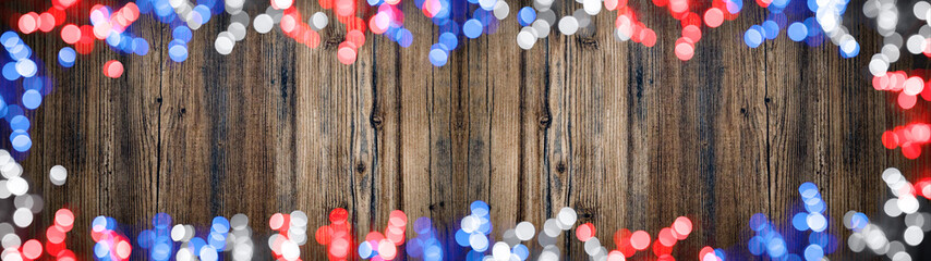 Frame made of red, blue, white bokeh lights (colors of the flag from america) on dark brown wooden texture, with space for text