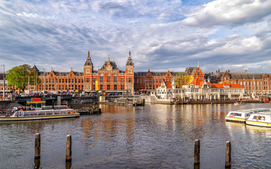Obraz premium Panoramic view of Central Train Station in Amsterdam, architecture monument built in 1889, city's main public transportation hub. Canal with ferry boats in the foreground. Amsterdam, Netherlands.