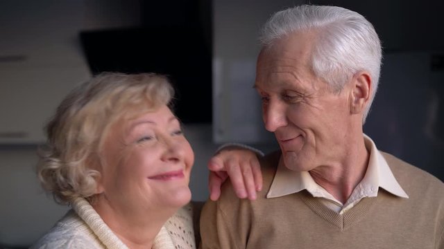 Nostalgic elderly couple smiling and hugging at home, nice memories about past